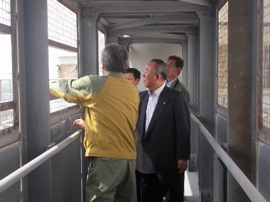 建物内の窓際で聖籠町長や関係者2名に説明を行っている作業服姿の男性の写真