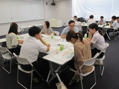 長テーブルを3台組み合わせて6名ほどのグループで座り資料を見ながら話をしている写真