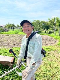 畑の草刈りをしている80歳代男性の写真